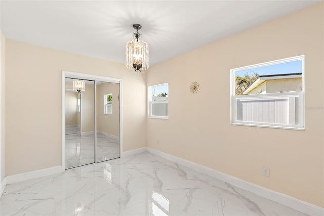 unfurnished bedroom with a closet, marble finish floor, baseboards, and an inviting chandelier