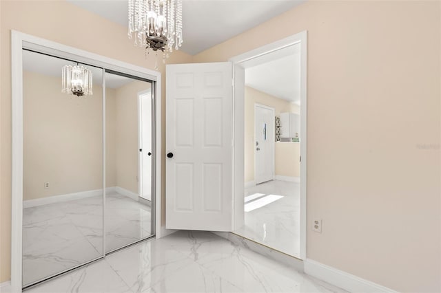 unfurnished bedroom with a notable chandelier, baseboards, marble finish floor, and a closet