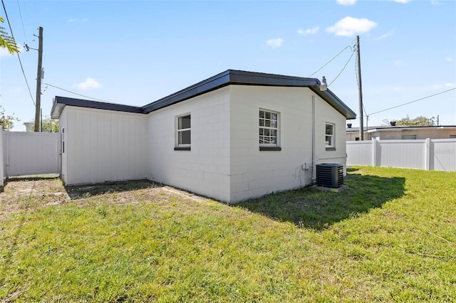 view of side of property featuring a lawn, central AC, concrete block siding, and fence