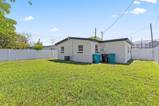 rear view of property with central air condition unit, a gate, a lawn, and a fenced backyard