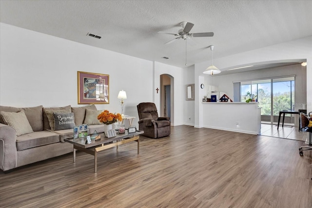 living room with arched walkways, visible vents, a textured ceiling, and wood finished floors