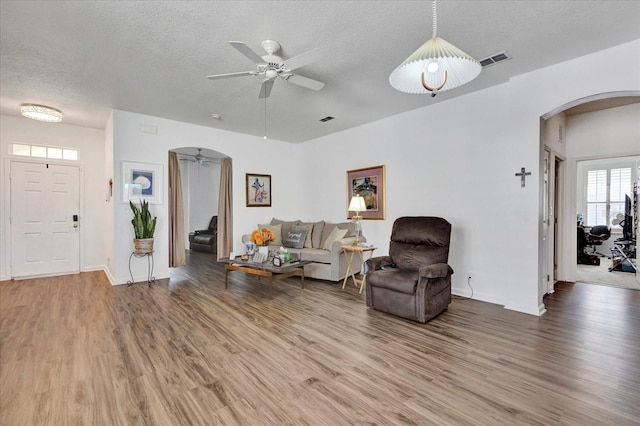 living area featuring visible vents, arched walkways, ceiling fan, a textured ceiling, and light wood-type flooring