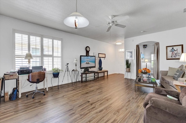 living area with arched walkways, a textured ceiling, ceiling fan, and wood finished floors