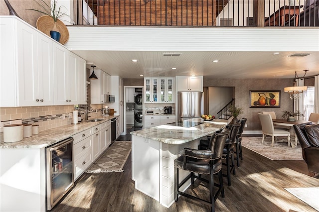 kitchen with a sink, a kitchen island, beverage cooler, freestanding refrigerator, and dark wood-style flooring