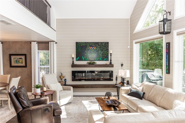 living room featuring a glass covered fireplace, a healthy amount of sunlight, and a towering ceiling