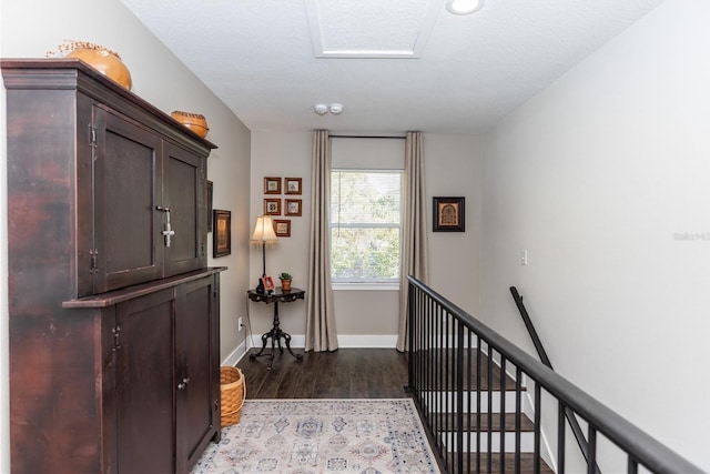 corridor featuring dark wood-style floors, an upstairs landing, and baseboards