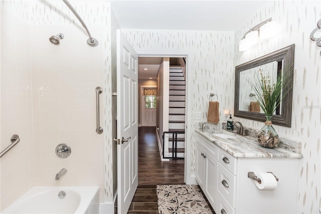 bathroom with wallpapered walls, bathing tub / shower combination, wood finished floors, and vanity