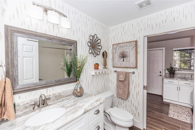 bathroom featuring vanity, wood finished floors, visible vents, wallpapered walls, and toilet