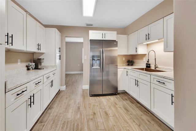 kitchen featuring visible vents, light wood-style flooring, white cabinets, stainless steel fridge, and a sink