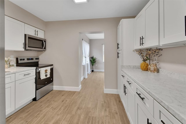 kitchen with light wood finished floors, baseboards, light stone countertops, appliances with stainless steel finishes, and white cabinetry