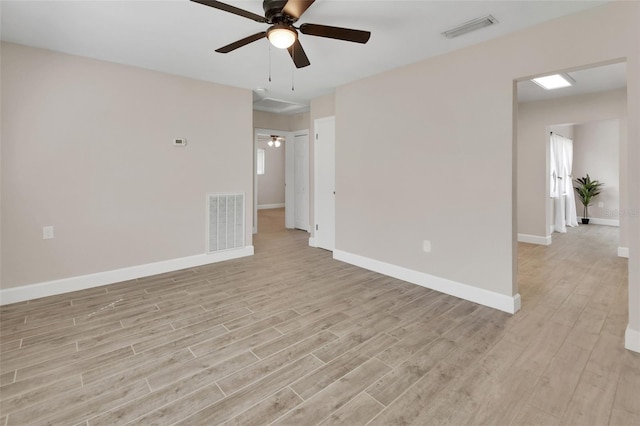 spare room with light wood finished floors, visible vents, a ceiling fan, and baseboards