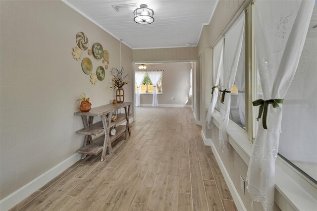 hallway with light wood-style flooring, crown molding, and baseboards