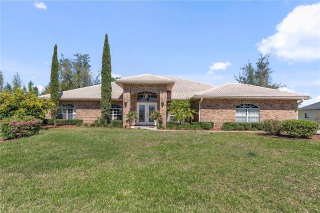 mediterranean / spanish home featuring a front lawn, a tiled roof, french doors, and brick siding