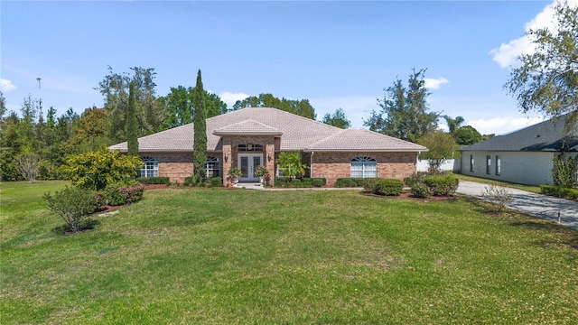 single story home featuring a front yard, driveway, french doors, a tiled roof, and brick siding