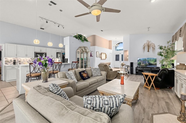 living room with a healthy amount of sunlight, a ceiling fan, light wood-type flooring, and a towering ceiling