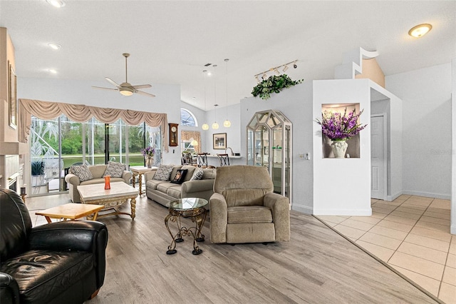 living area with light wood finished floors, high vaulted ceiling, baseboards, and a ceiling fan