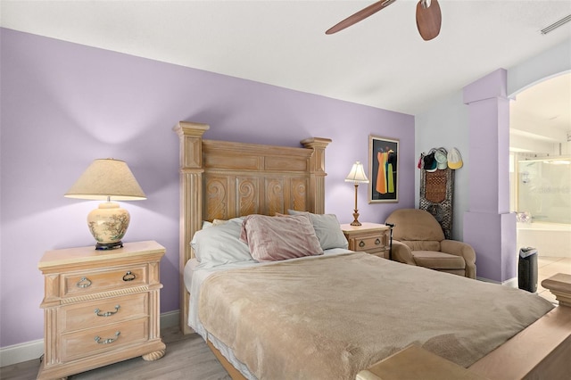 bedroom with visible vents, connected bathroom, arched walkways, light wood-style floors, and baseboards