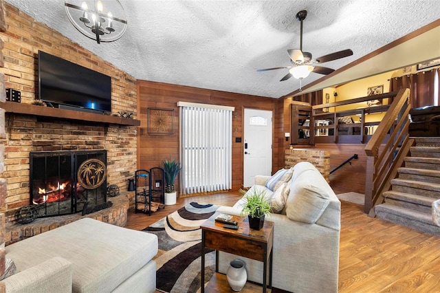 living room featuring a brick fireplace, vaulted ceiling, ceiling fan with notable chandelier, wood finished floors, and a textured ceiling