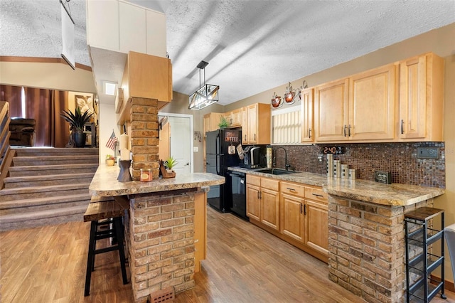 kitchen featuring light brown cabinetry, black appliances, a breakfast bar area, and a sink