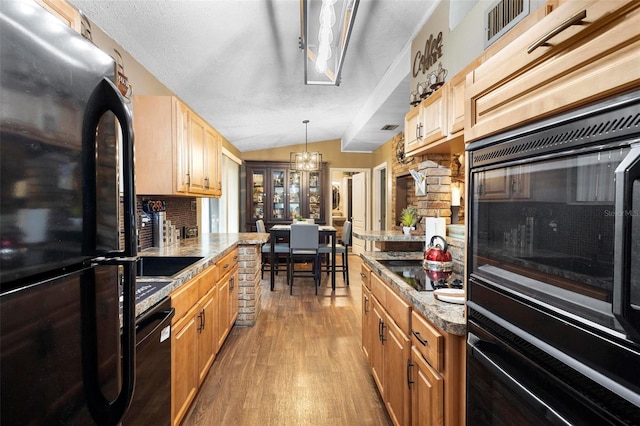 kitchen featuring visible vents, black appliances, backsplash, wood finished floors, and lofted ceiling