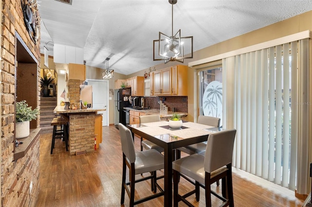 dining area with lofted ceiling, a notable chandelier, light wood-style floors, and a textured ceiling