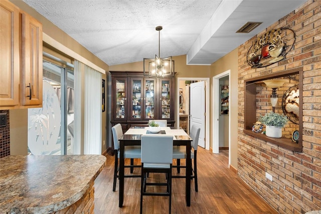 dining room with visible vents, lofted ceiling, a textured ceiling, and wood finished floors