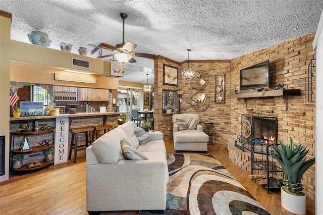 living room with wood finished floors, visible vents, a fireplace, ceiling fan, and a textured ceiling