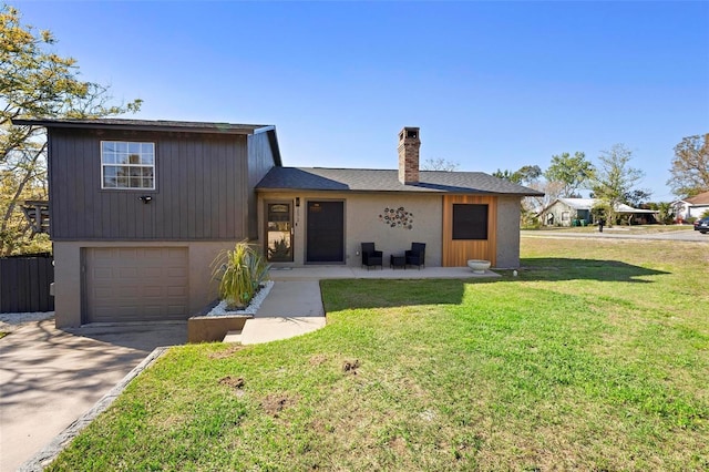 split level home featuring stucco siding, driveway, a front yard, a garage, and a chimney