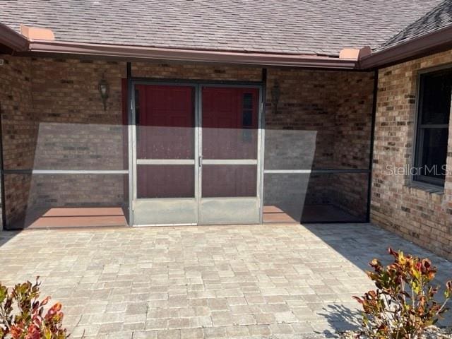 doorway to property with brick siding and roof with shingles