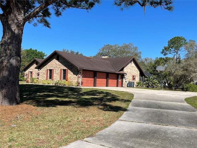 view of front of home featuring cooling unit, driveway, an attached garage, a chimney, and a front lawn