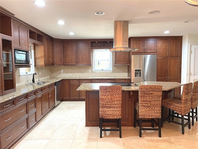 kitchen with a sink, backsplash, appliances with stainless steel finishes, a breakfast bar area, and island range hood