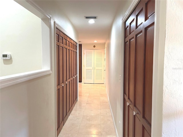 hall featuring light tile patterned floors, visible vents, and baseboards