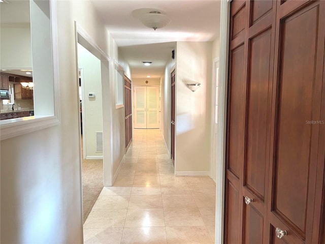 corridor with light tile patterned floors, visible vents, baseboards, and light carpet