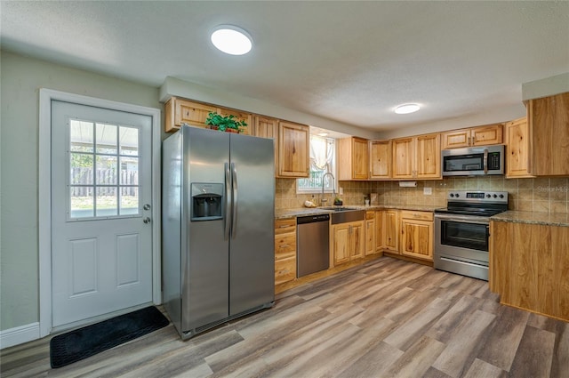 kitchen featuring light wood-style floors, tasteful backsplash, appliances with stainless steel finishes, and a sink