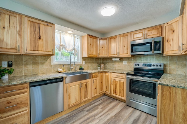 kitchen with a sink, light stone counters, backsplash, light wood-style floors, and appliances with stainless steel finishes