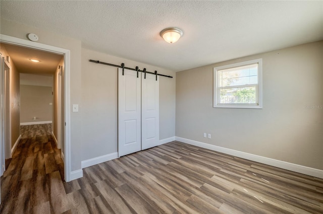 unfurnished bedroom featuring a textured ceiling, wood finished floors, a barn door, a closet, and baseboards