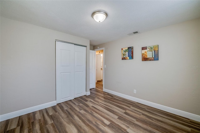 unfurnished bedroom with visible vents, a textured ceiling, wood finished floors, a closet, and baseboards