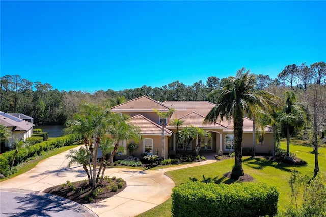 mediterranean / spanish-style home with curved driveway, a tiled roof, a front yard, and stucco siding