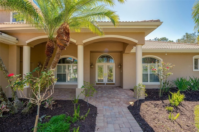 property entrance featuring a tile roof, french doors, and stucco siding