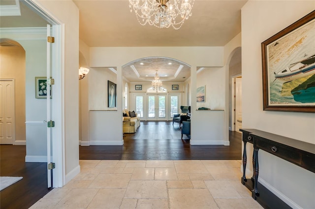 entryway with arched walkways, a notable chandelier, stone tile floors, and a raised ceiling