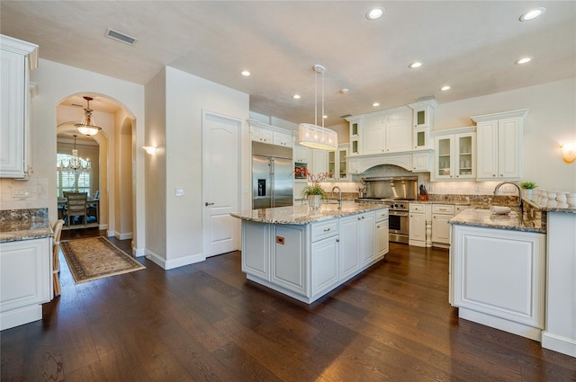 kitchen featuring a notable chandelier, a kitchen island with sink, premium appliances, arched walkways, and decorative backsplash