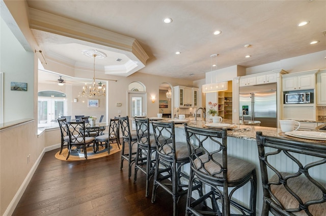 kitchen featuring a kitchen bar, a tray ceiling, dark wood finished floors, crown molding, and built in appliances