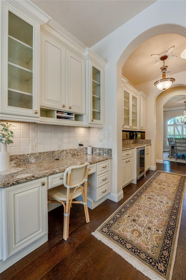 kitchen with backsplash, wine cooler, light stone counters, arched walkways, and dark wood-style flooring