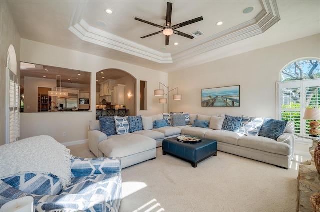 living area with ornamental molding, a ceiling fan, arched walkways, carpet flooring, and a raised ceiling