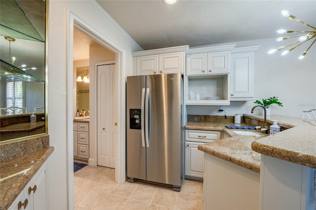 kitchen with light stone counters, white cabinets, a notable chandelier, stainless steel fridge, and open shelves