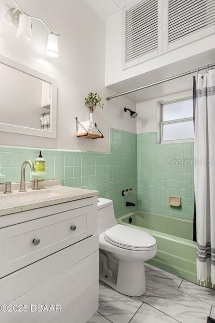 bathroom featuring toilet, vanity, marble finish floor, tile walls, and shower / bathtub combination with curtain