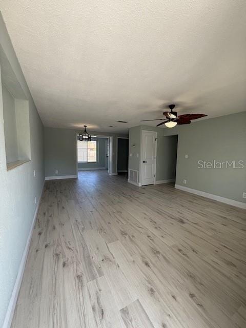 unfurnished living room featuring baseboards, ceiling fan with notable chandelier, light wood-type flooring, and a textured ceiling