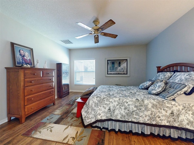 bedroom featuring visible vents, ceiling fan, baseboards, wood finished floors, and a textured ceiling