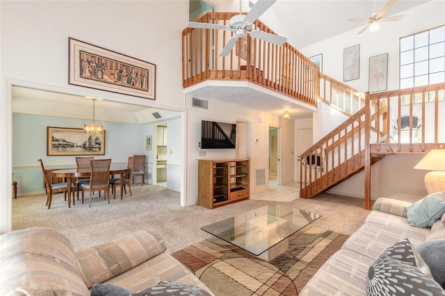 carpeted living room featuring stairway, ceiling fan with notable chandelier, a high ceiling, and visible vents