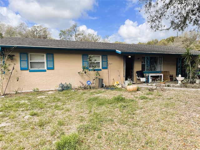 single story home with a front lawn, concrete block siding, and a shingled roof